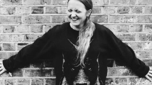 Image of Hollie McNish with her back to a brick wall, laughing
