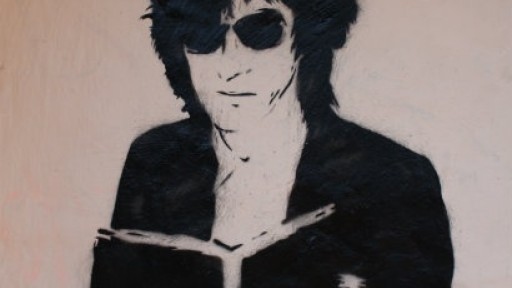Black and white Banksy-style graffiti image of John Cooper Clark reading a book