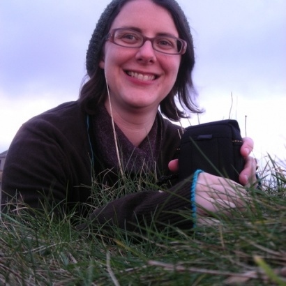 A picture of MLF Children and Young People's Coordinator Liz Postlethwaite sitting in a field, smiling, wearing headphones