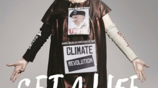 Image of Vivienne Westwood in a long dark smock, with a sign reading 'Climate Revolution' pinned to her front, and her arms outstretched