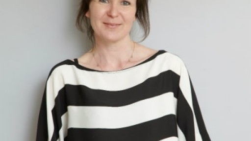 Image of Olivia Laing leaning against a white wall, wearing a loose black and white striped shirt