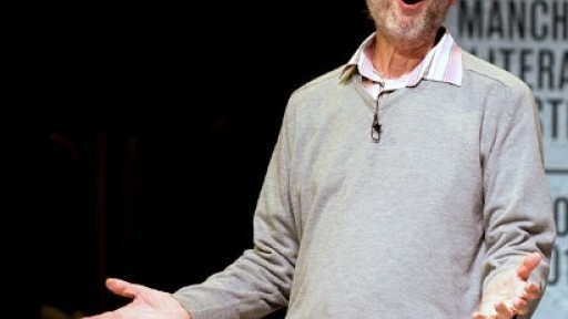 Image of Michael Rosen on stage, looking amused with his hands outstretched