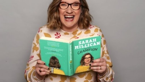Comedian and author Sarah Millican smiling whilst holding her debut book!