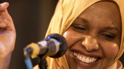 Image of Asha Lul Mohamud Yusuf wearing a yellow headscarf and laughing in front of a microphone