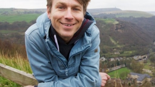 Image of Ben Faulks in a blue cagoule, leaning on a wooden fence in the countryside