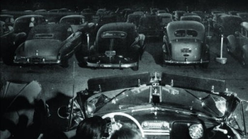 Black and white image of a young couple in a car at an old American drive-in cinema