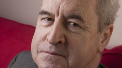 Image of John Banville, looking serious on a red sofa