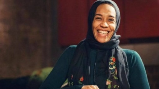Image of a laughing Asma Elbadawi, wearing a black headscarf with embroidered rose flowers and leavers