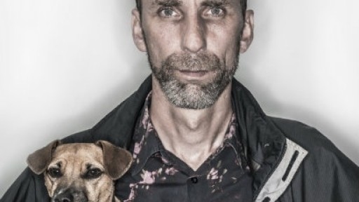 A serious-looking mugshot of Will Self, holding a jack russell dog under one arm