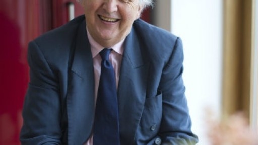 Head and shoulders shot of Alexander McCall Smith, sitting at a table with a cup of tea in front of him