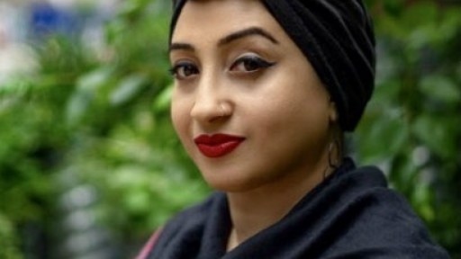 Headshot of Hafsah Aneela Bashir, wearing a black turban with foliage behind her