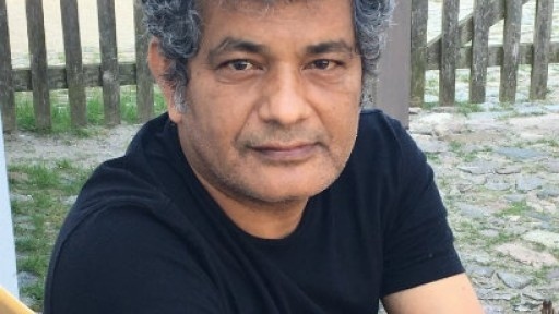 Headshot of Mohammed Hanif, sitting on a wooden bench with a fence in the background