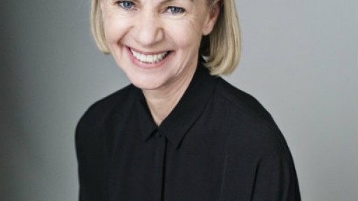Head and shoulders photo of author Kate Mosse smiling broadly, wearing a black shirt against a grey background