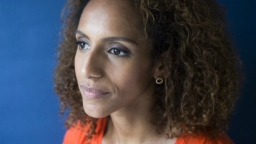 Head and shoulders image of Afua Hirsch wearing an orange top against a bright blue background