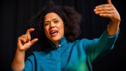 Image of Rommi Smith in front of a dark background, with her hands are in the air gesticulating