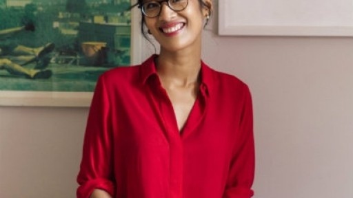 Head and shoulders shot of author Elaine Castillo, seated in a chair, smiling and wearing a red shirt