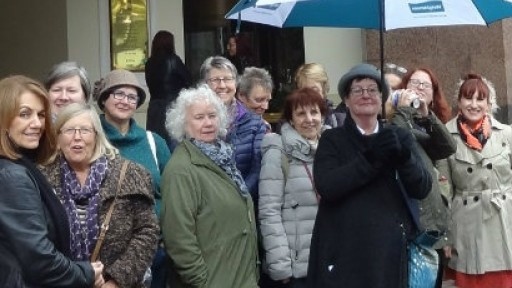 Image of walking tour host, Anne Beswick, surrounded by tour participants, under a large umbrella