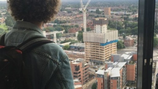 Shot taken from behind a young person looking out the window over the skyline of Manchester