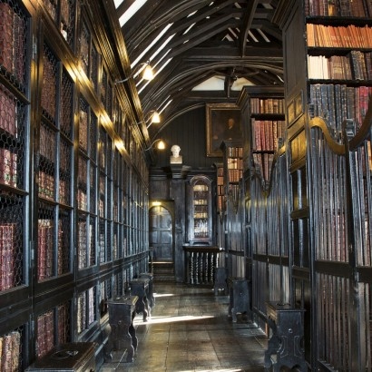 Atmospheric photo of a corridor lined with black bookshelves and fabric bound hardbacks in the historic Chethams Library