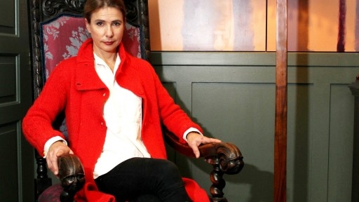 American author Lionel Shriver sat in a grand chair under a large bright red lamp.