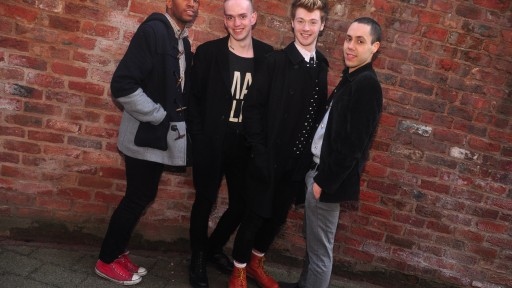 Group of 4 young queer performers and writers against a brick wall