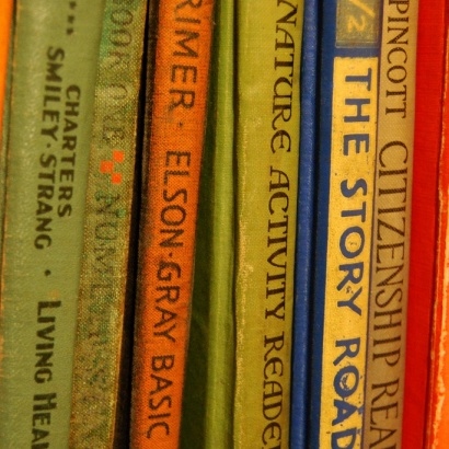 A row of vintage school books from various eras on a bookshelf in a variety of muted colours.